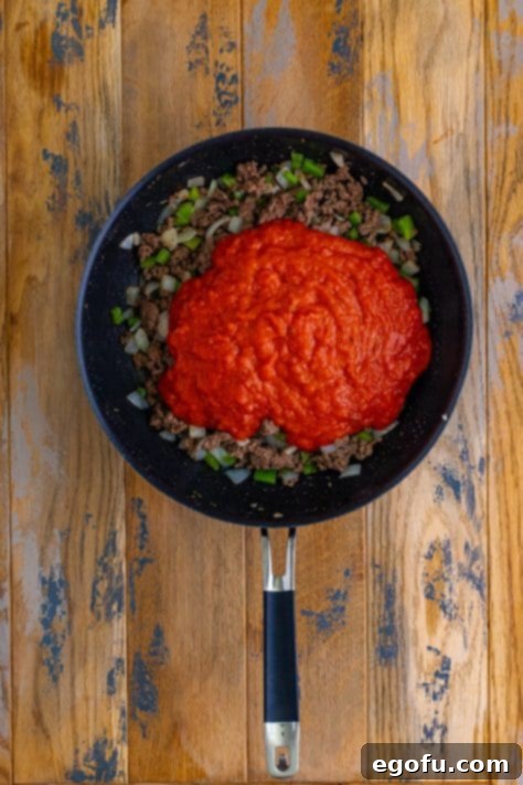 marinara sauce added to cooked ground beef in a large skillet.