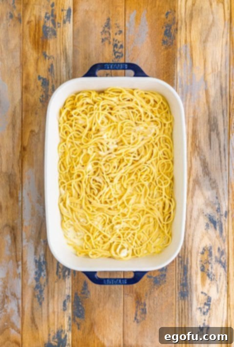 A baking dish with cooked spaghetti in a cream butter sauce.