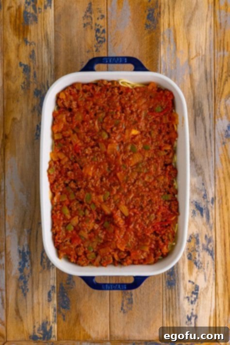 meat sauce spread evenly over spaghetti noodles in a casserole dish.