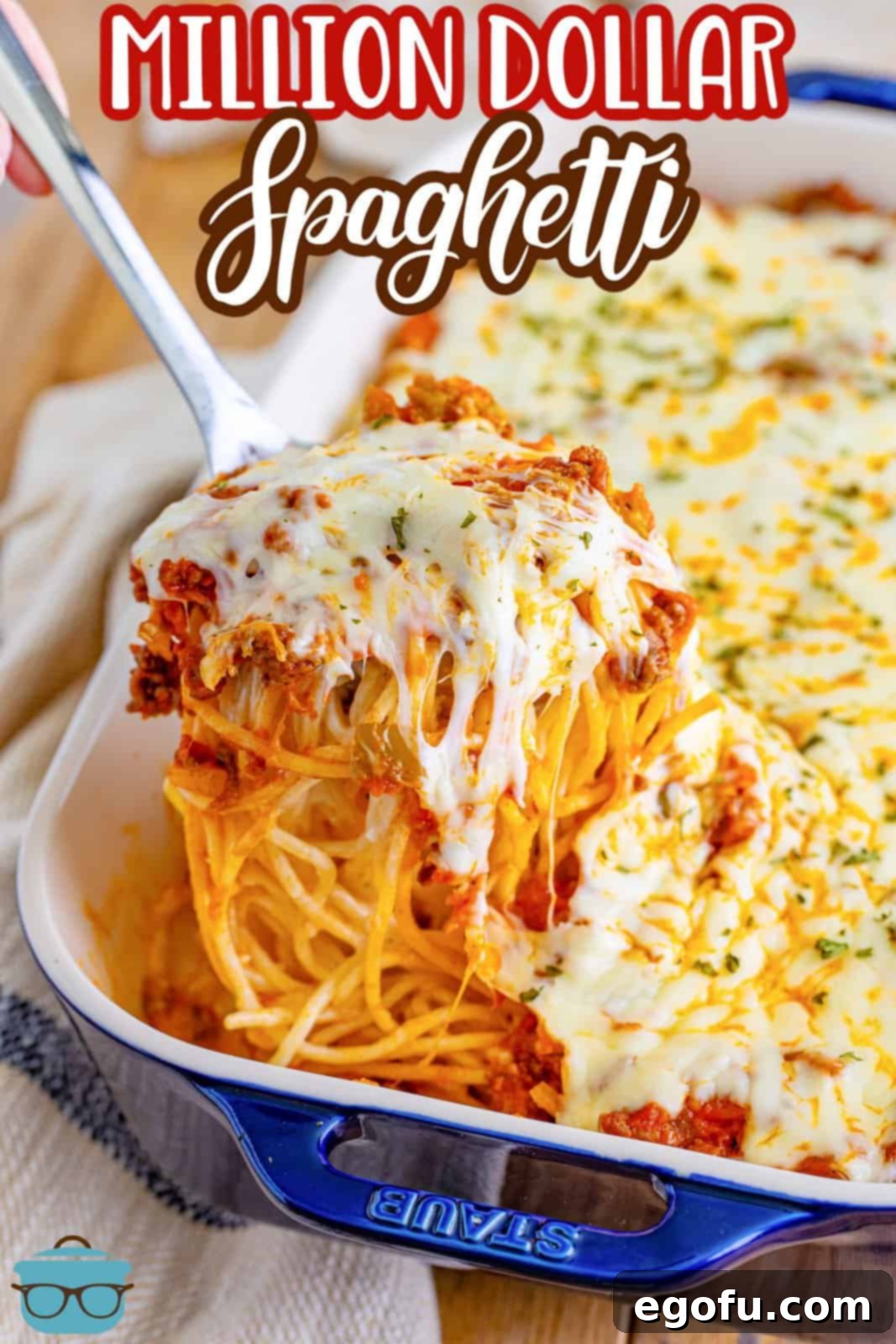 A large silver spoon carefully scooping a generous portion of Million Dollar Spaghetti from a deep casserole dish, revealing the enticing layers within.
