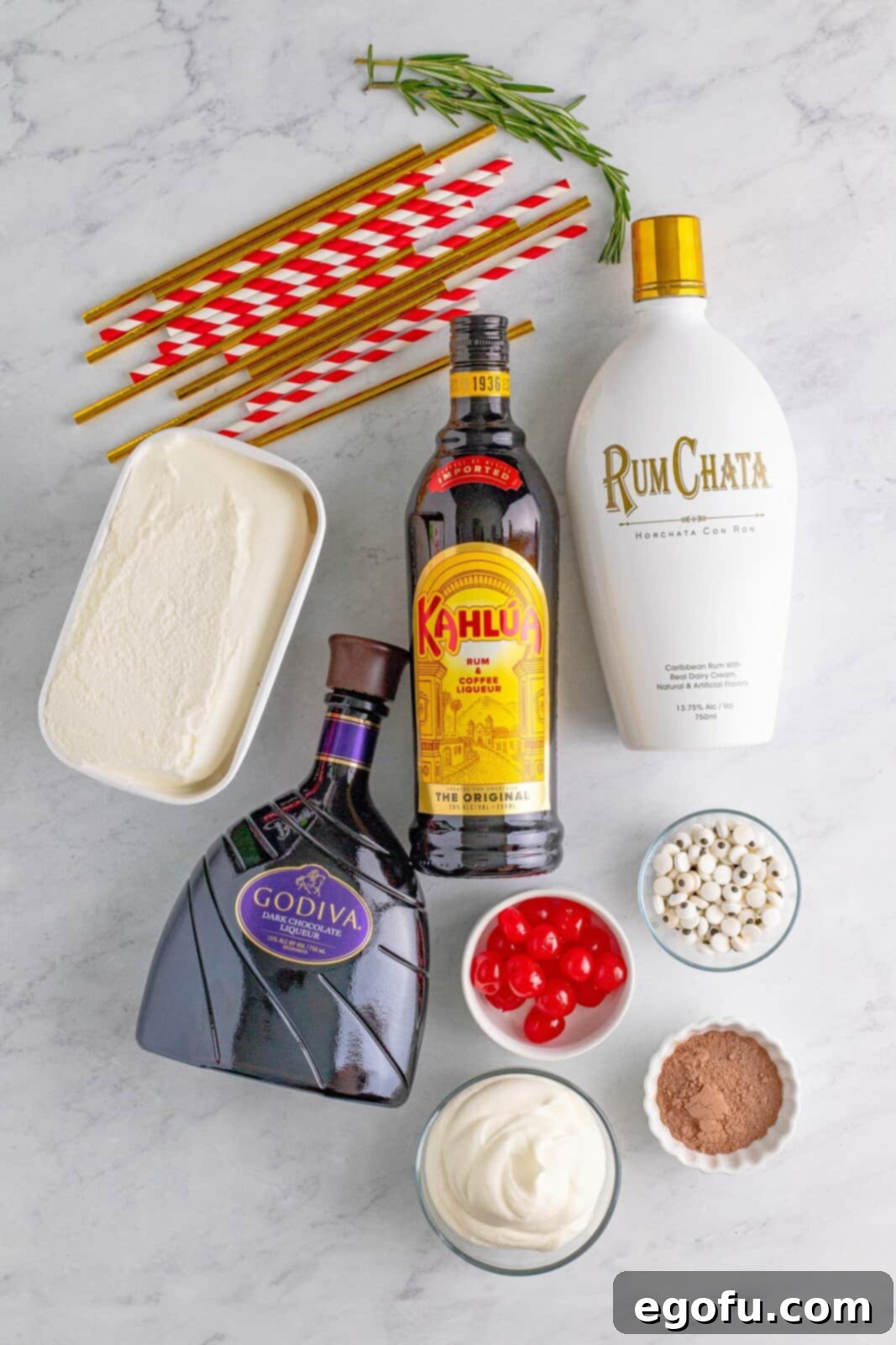 Rudolph on the Rocks 4 A flat lay of all the Drunken Rudolph milkshake ingredients: vanilla ice cream, Kahlua, RumChata, chocolate liquor, hot cocoa mix, maraschino cherries, whipped cream, and candy eyes, artfully arranged on a surface.