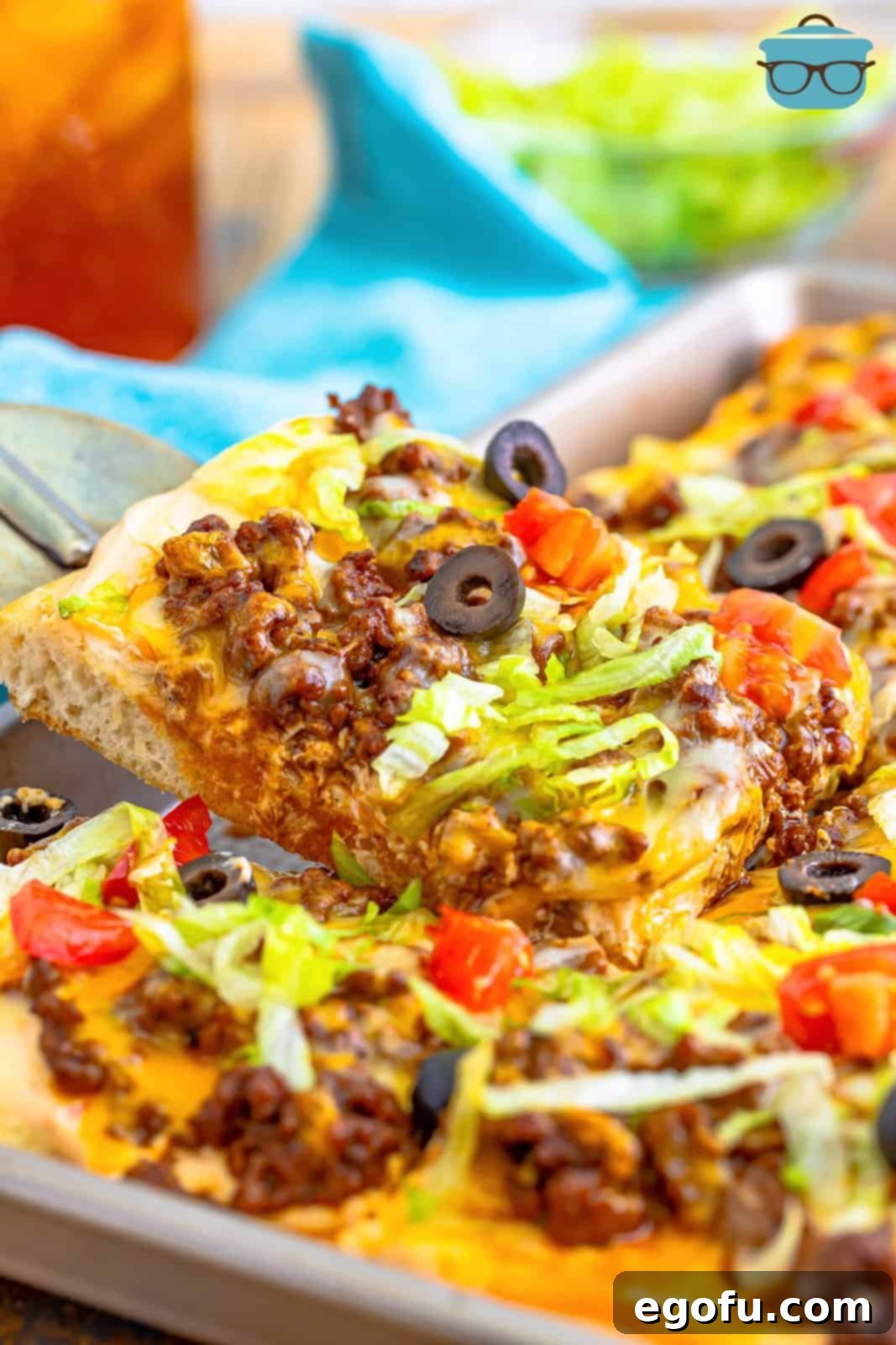 A spatula lifting up a square slice of Taco Pizza from a baking pan, showcasing its delicious layers and vibrant toppings.
