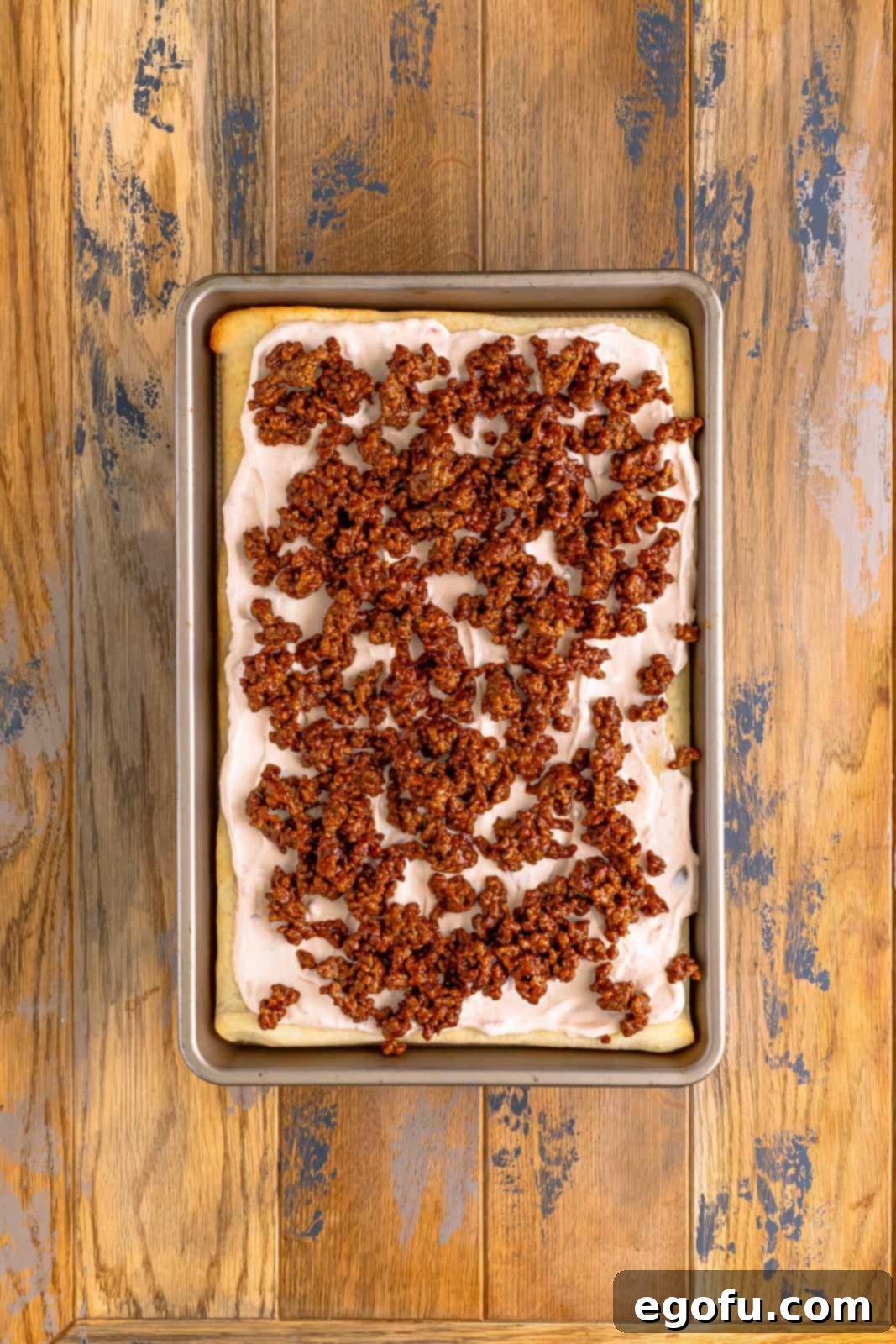 Seasoned taco meat evenly sprinkled on top of the cream cheese layer on the pizza crust.