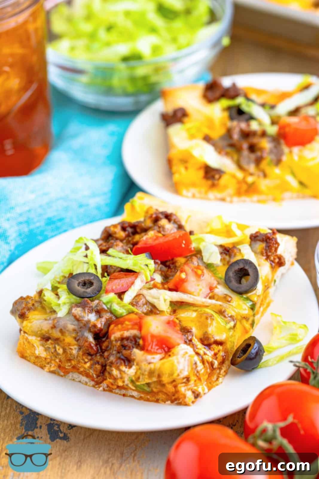 A perfectly cut slice of taco pizza presented on a round white plate, with a glass of iced tea in the background.