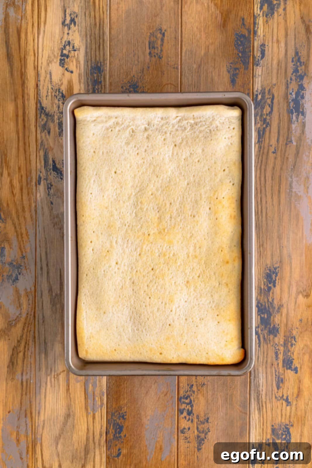 A rectangular baking pan holding a pre-baked pizza dough, light golden brown and ready for toppings.