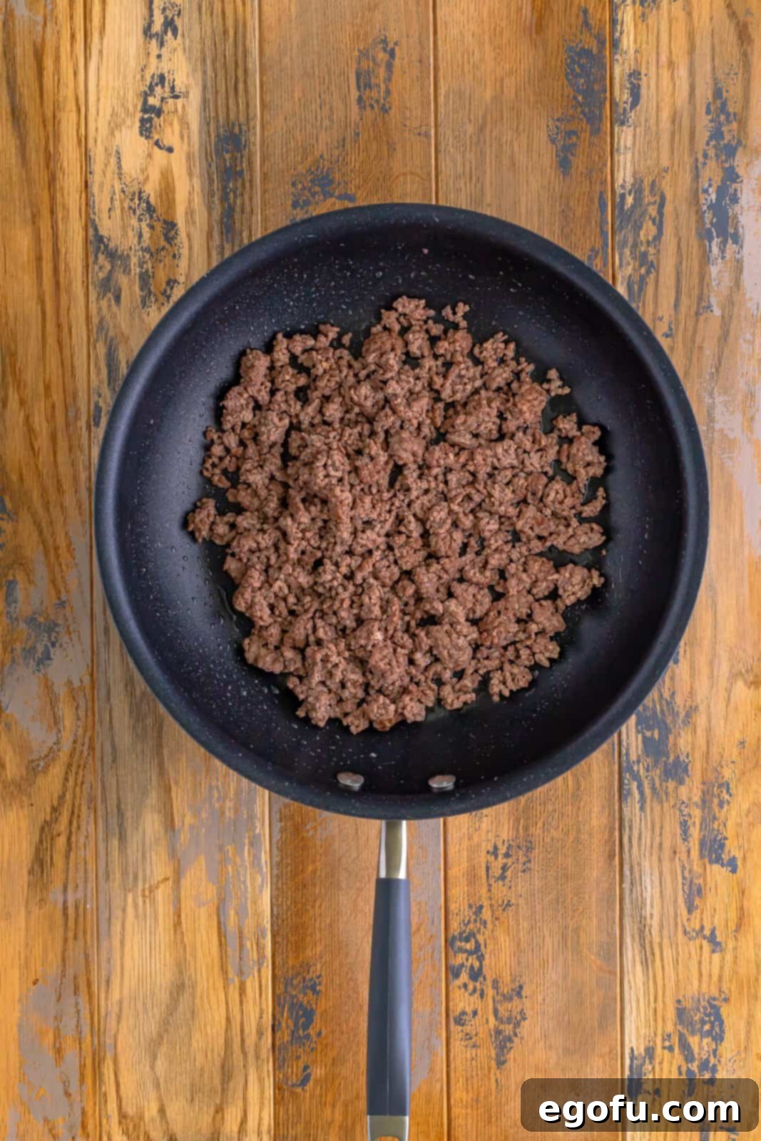 Cooked and crumbled ground beef resting in a skillet, thoroughly browned and ready for seasoning.