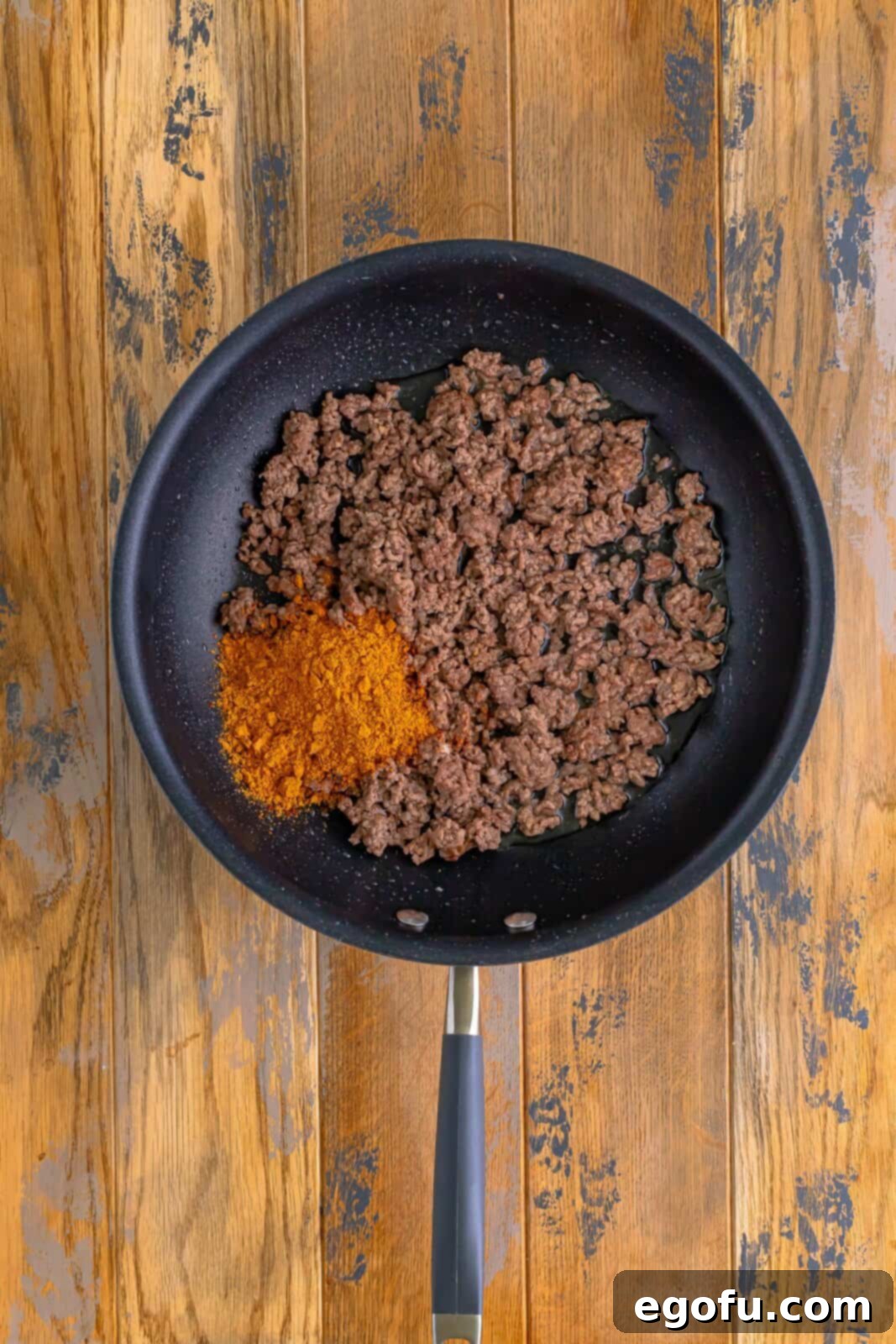 Taco seasoning and water stirred into the cooked ground beef in a skillet, creating a rich, flavorful mixture.