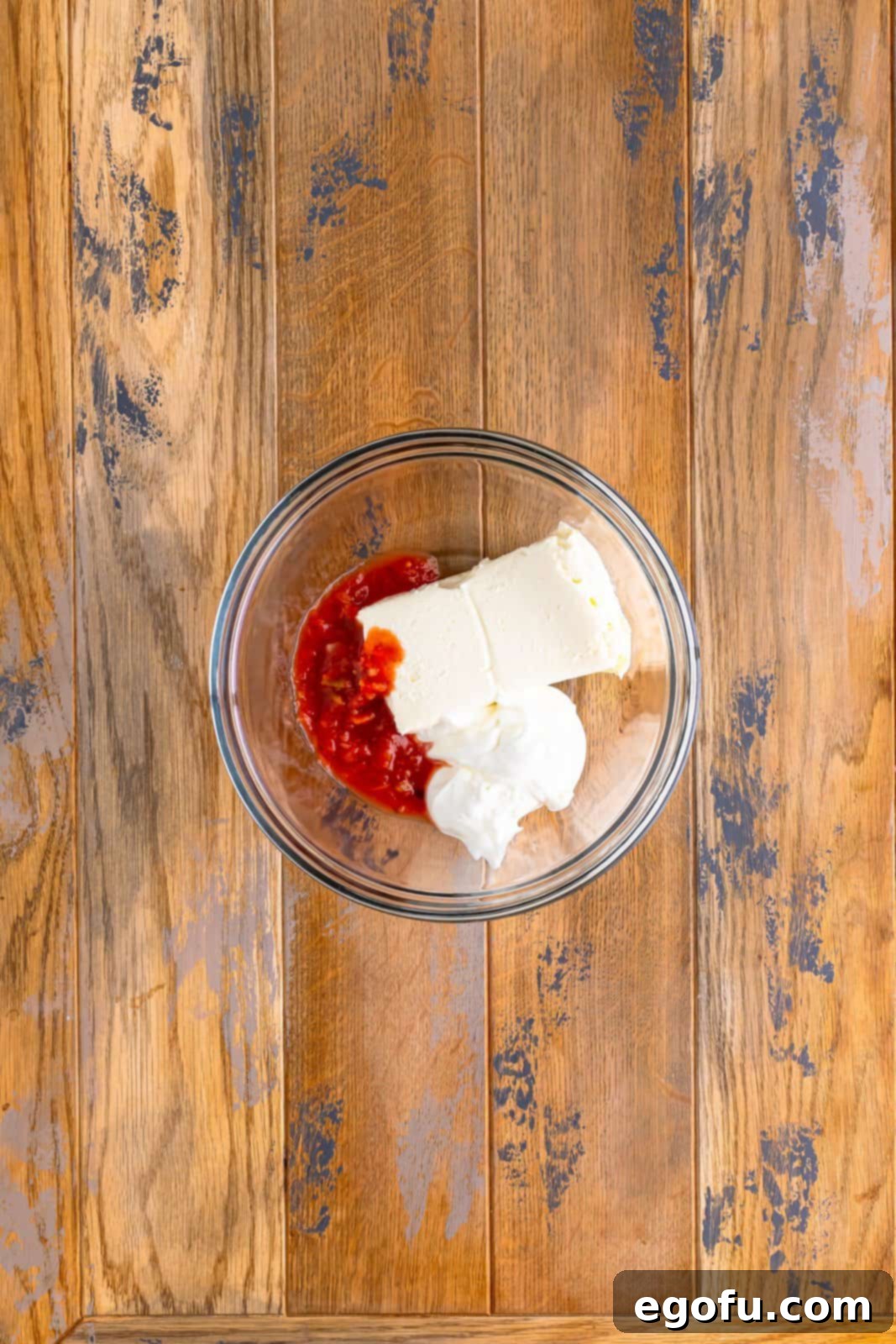 Cream cheese, sour cream, and salsa being mixed together in a clear bowl, forming a smooth and creamy sauce.