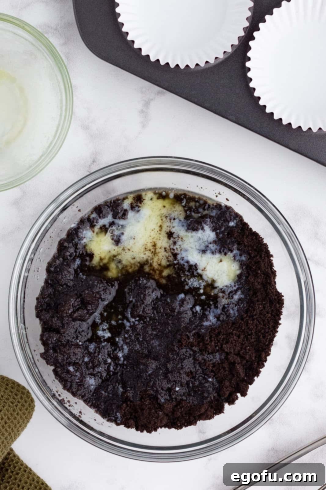 Oreo cookie crumbs combined with melted butter in a bowl.