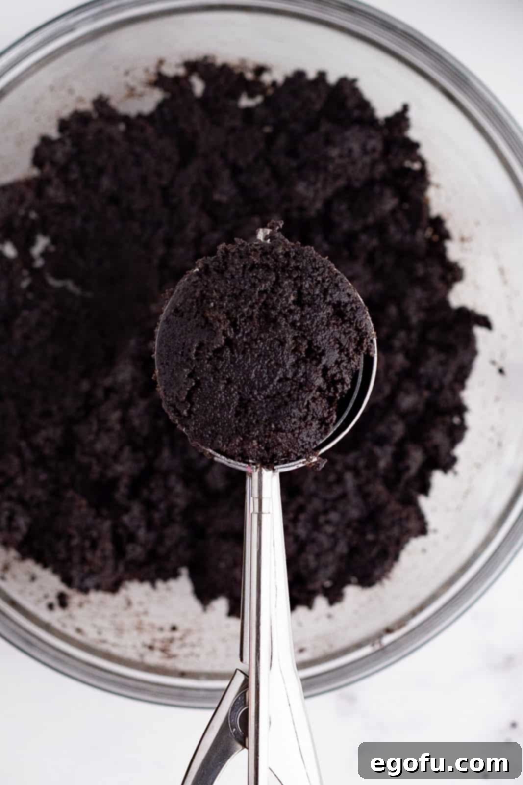 a cookie scoop scooping up some Oreo cookie crumb crust mixture out of a bowl.