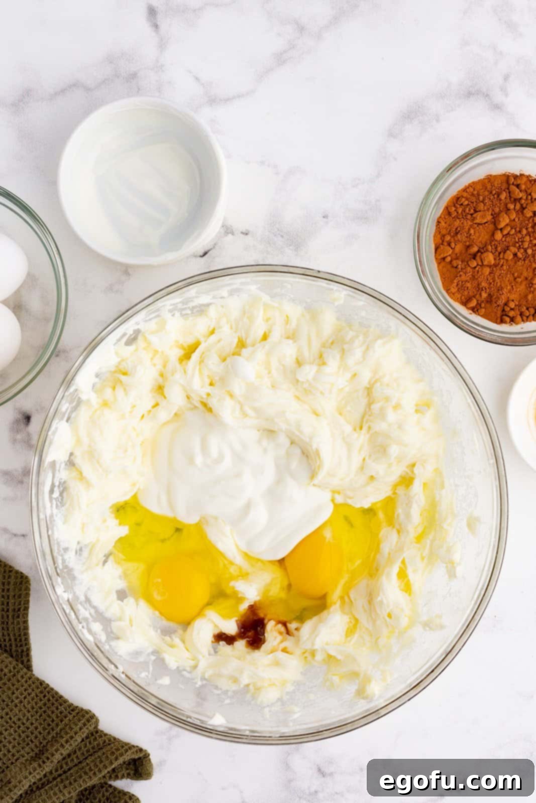 eggs and vanilla extract added to cream cheese mixture in a clear bowl.