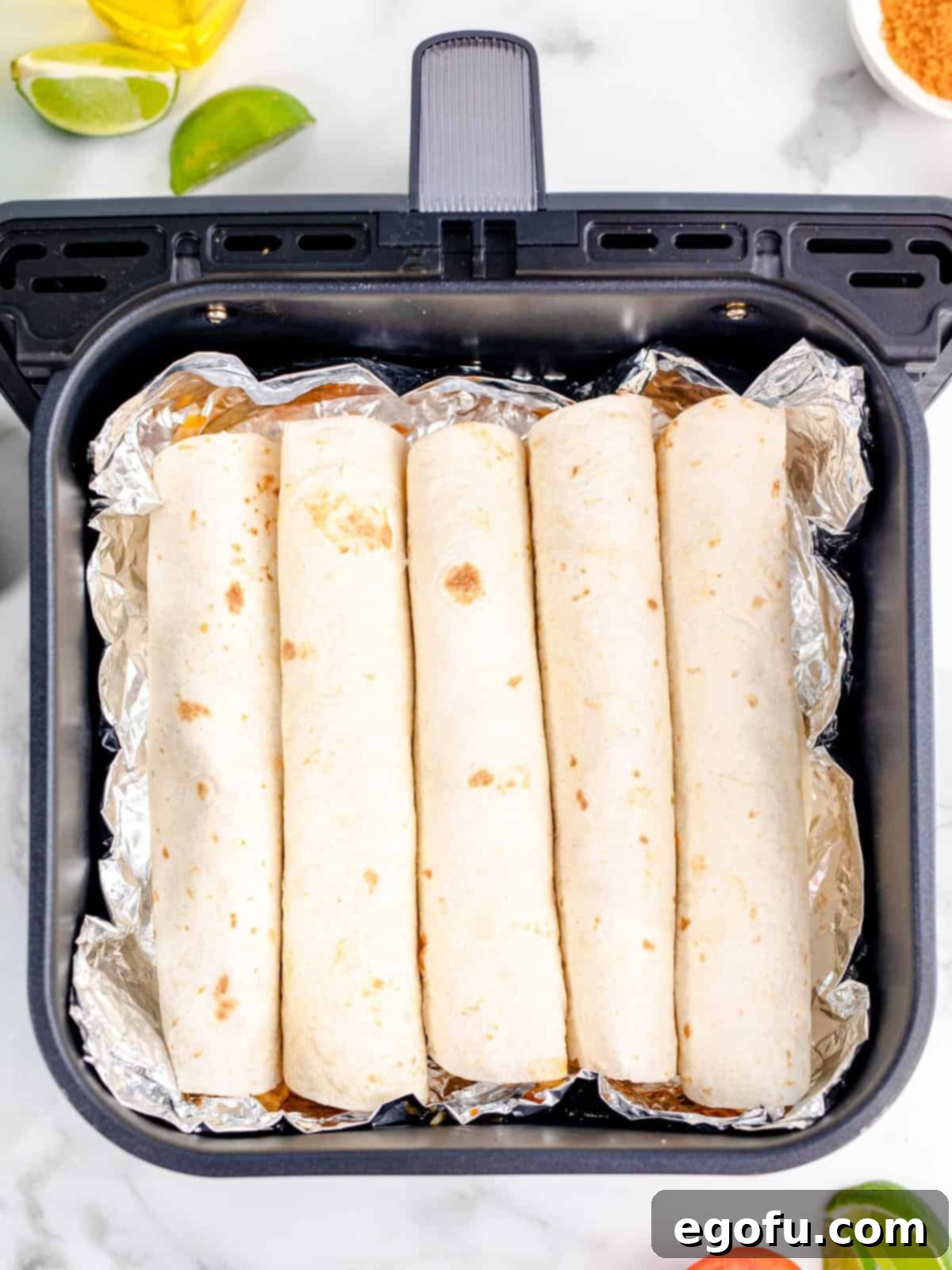 rolled up tortillas lined up and placed on the aluminum foil in the air fryer basket.