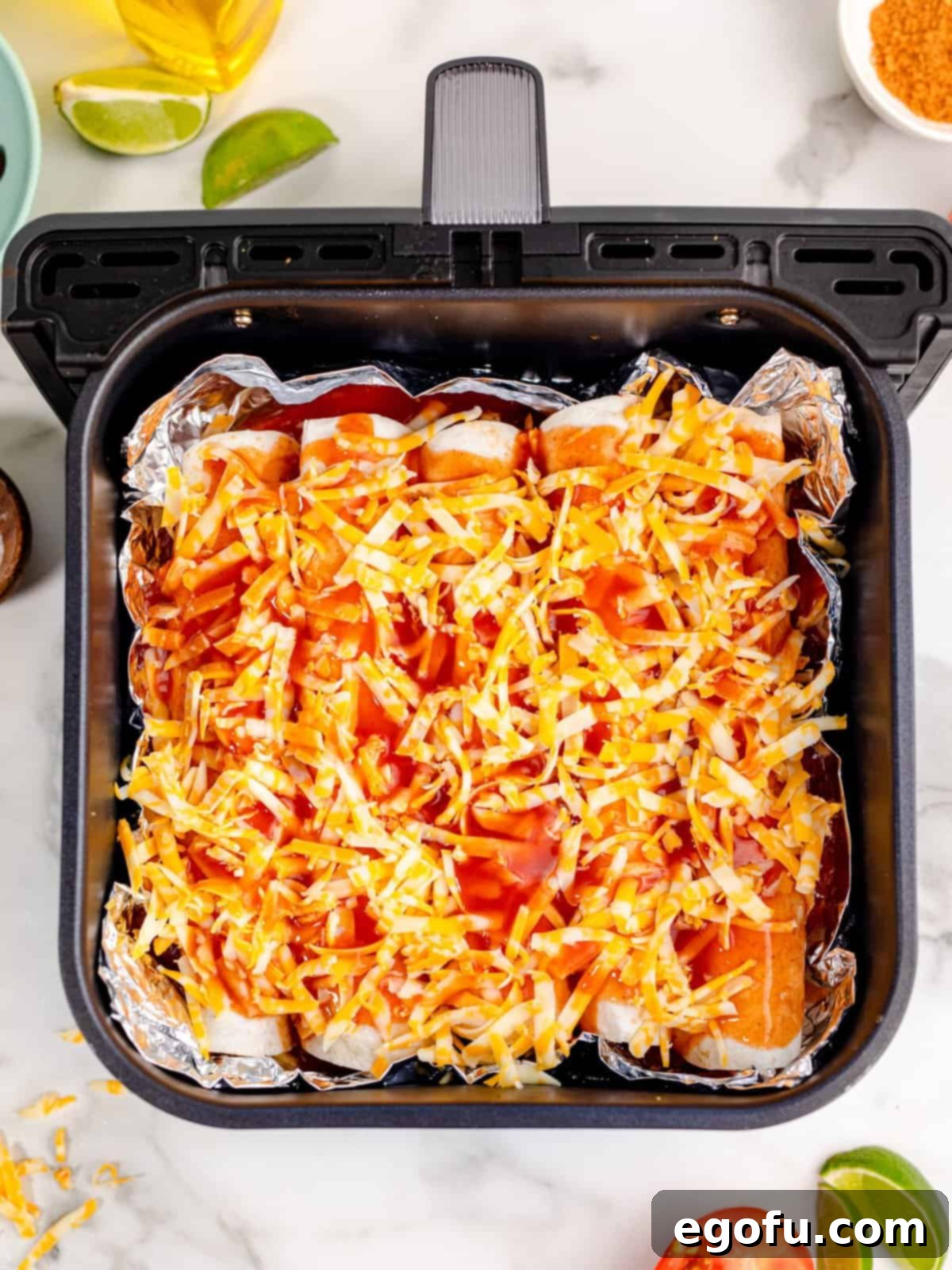 enchilada sauce and shredded cheese spread on top of rolled up flour tortillas.