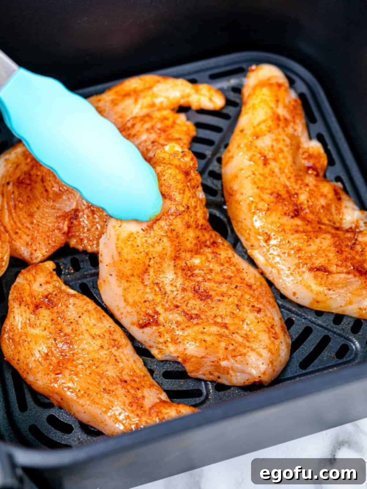 placing seasoned chicken breasts into an air fryer basket.