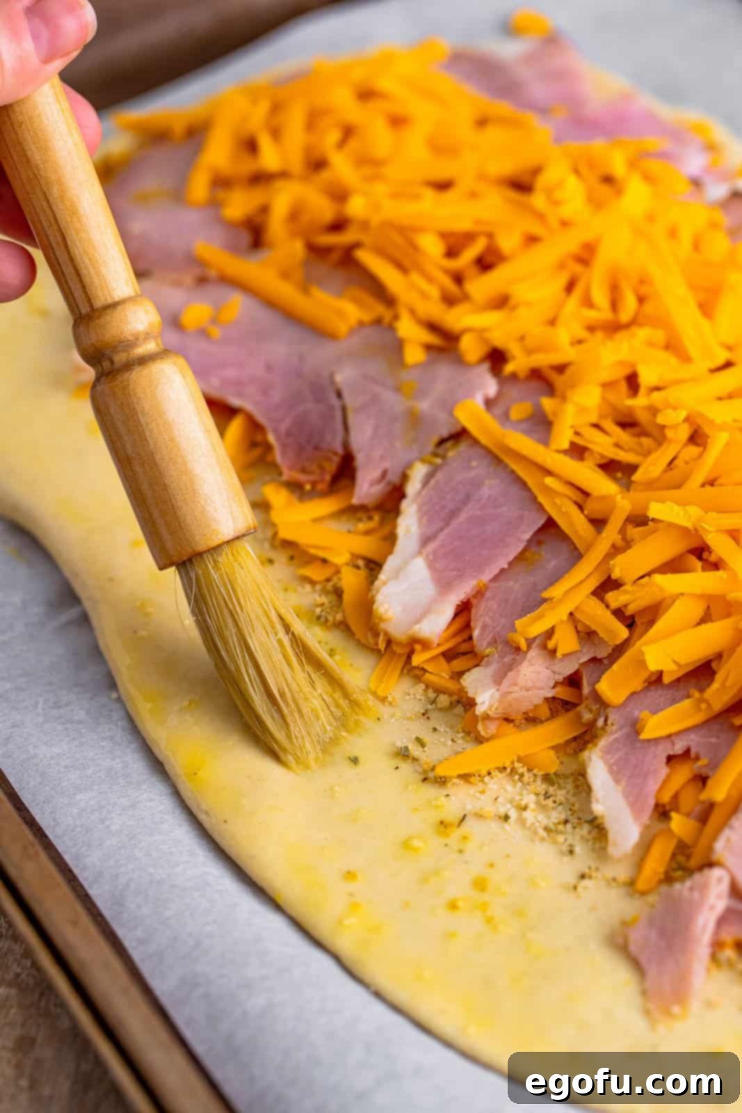 Effortless Ham and Cheese Stromboli Delight 12 pastry brush spreading egg was mixture around the edges of the pizza dough.