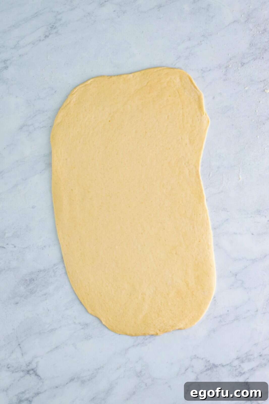 Effortless Ham and Cheese Stromboli Delight 5 rolled out pizza dough on a marble surface.