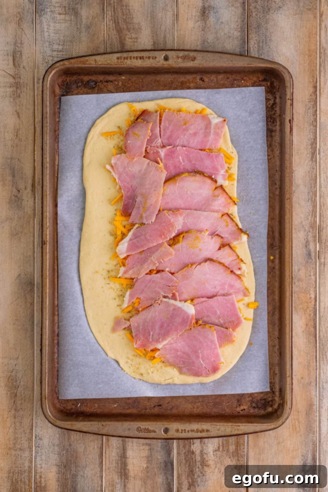 Effortless Ham and Cheese Stromboli Delight 10 sliced ham layered evenly over cheddar cheese on pizza dough.