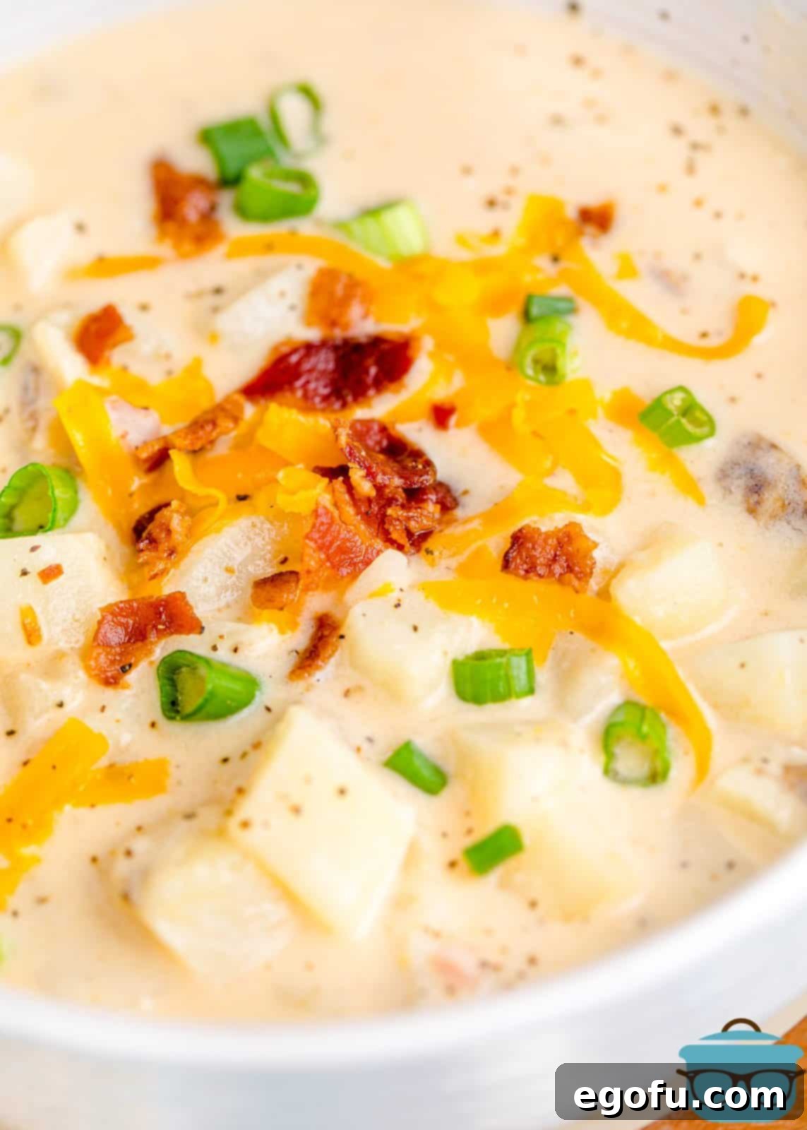 Effortless Slow Cooker Potato Soup with Frozen Potatoes 10 A close-up photo of a bowl filled with slow cooker potato soup, beautifully topped with crispy crumbled bacon, melted shredded cheddar cheese, and fresh sliced green onions.