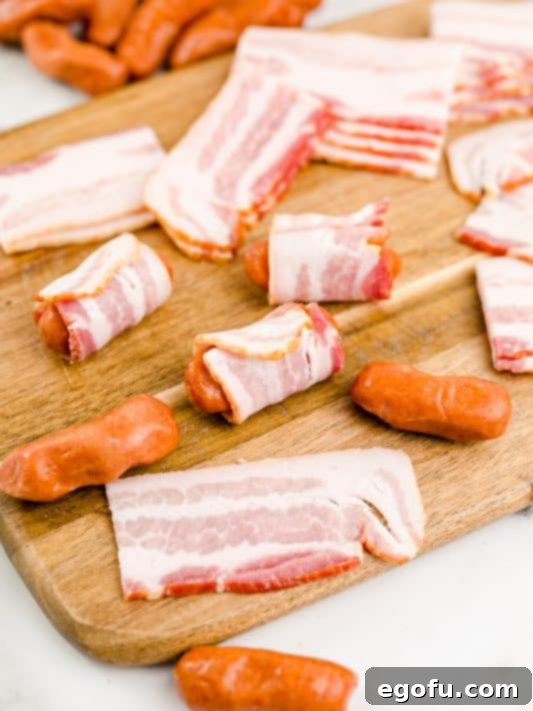 cocktail sausage shown being wrapped with a cut piece of bacon.