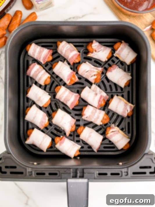 bacon wrapped sausages shown lined up in an air fryer basket.