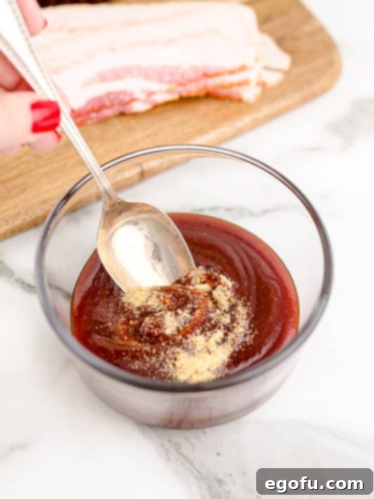 a spoon shown mixing together barbecue sauce and garlic powder in a small clear bowl.