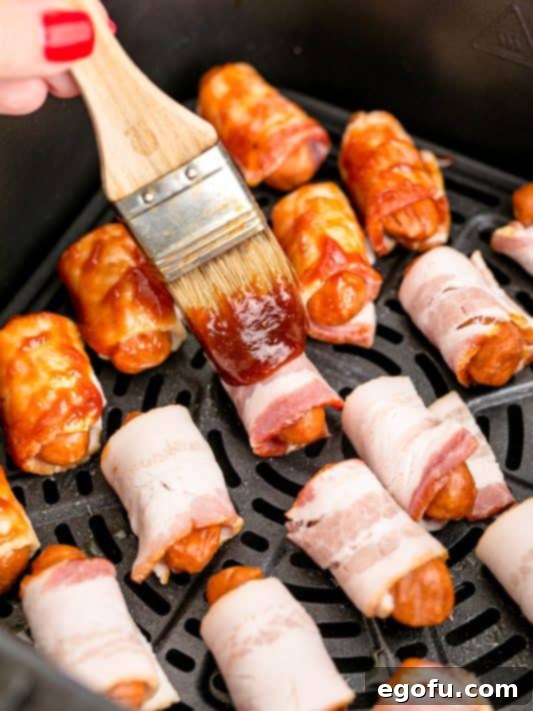 a pastry brush shown spreading barbecue sauce on top of the bacon wrapped sausages.