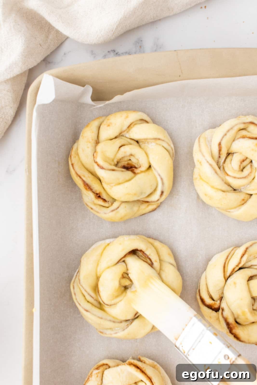 a pastry brush brushing a cinnamon knot with an egg wash. 