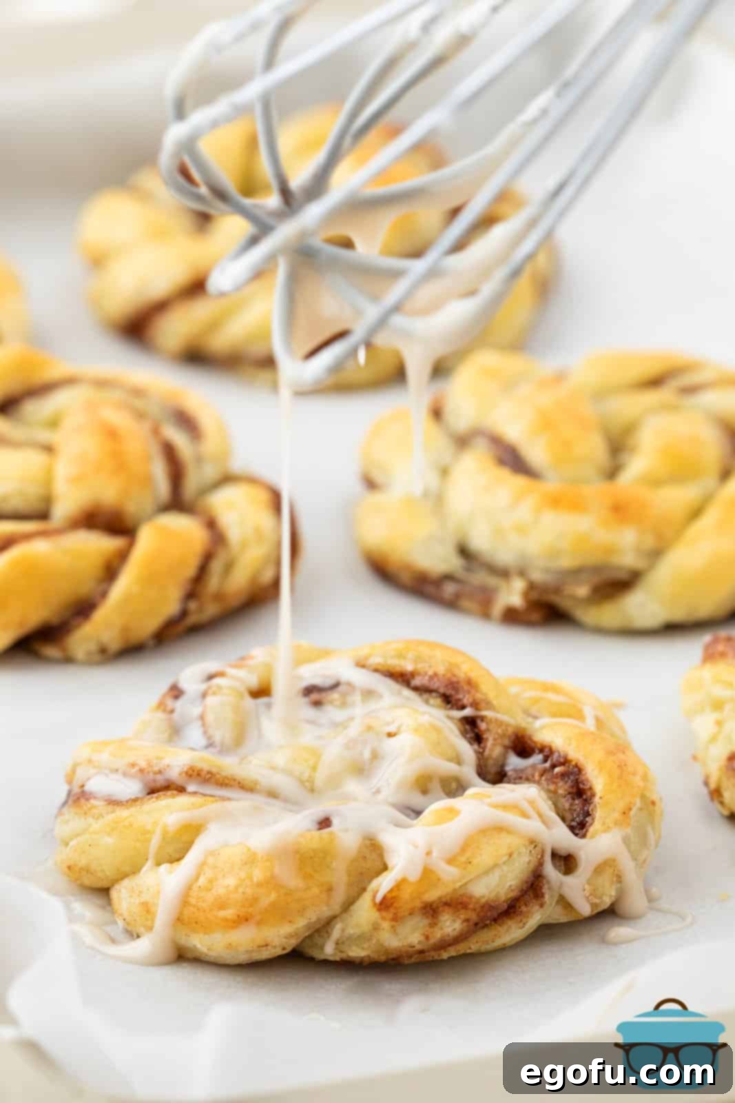 a whisk shown drizzling a powdered sugar icing over the cinnamon knots. 