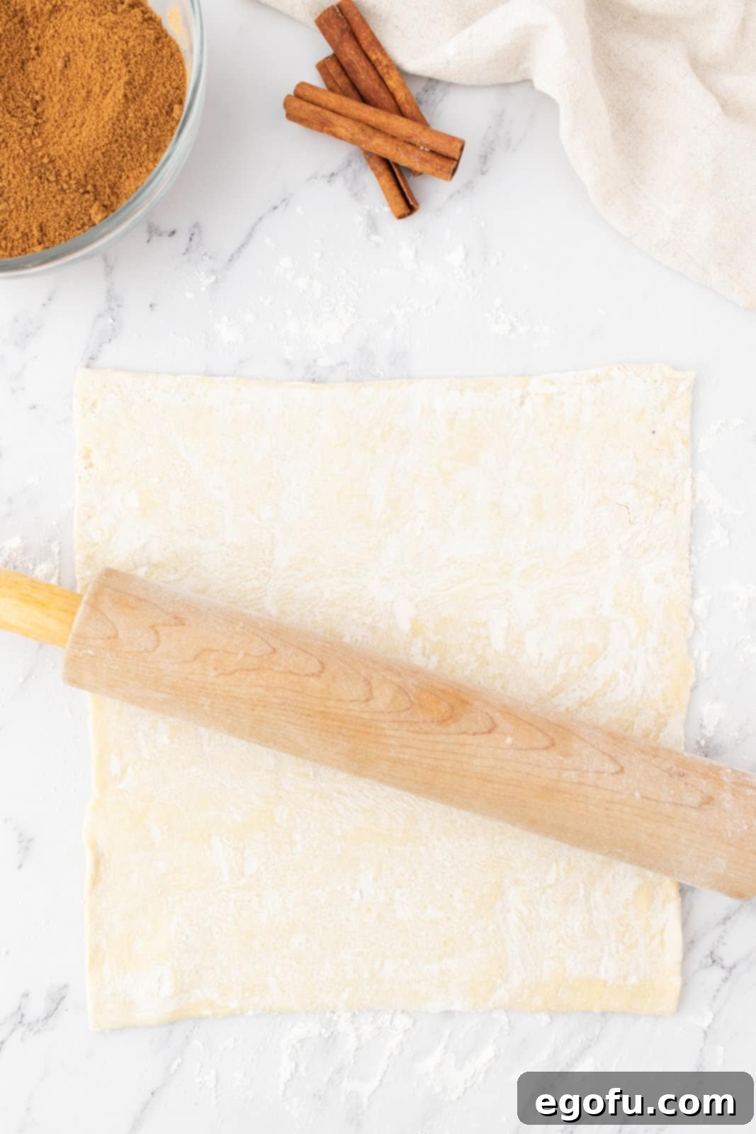 rolling out a sheet of puff pastry with a rolling pin.