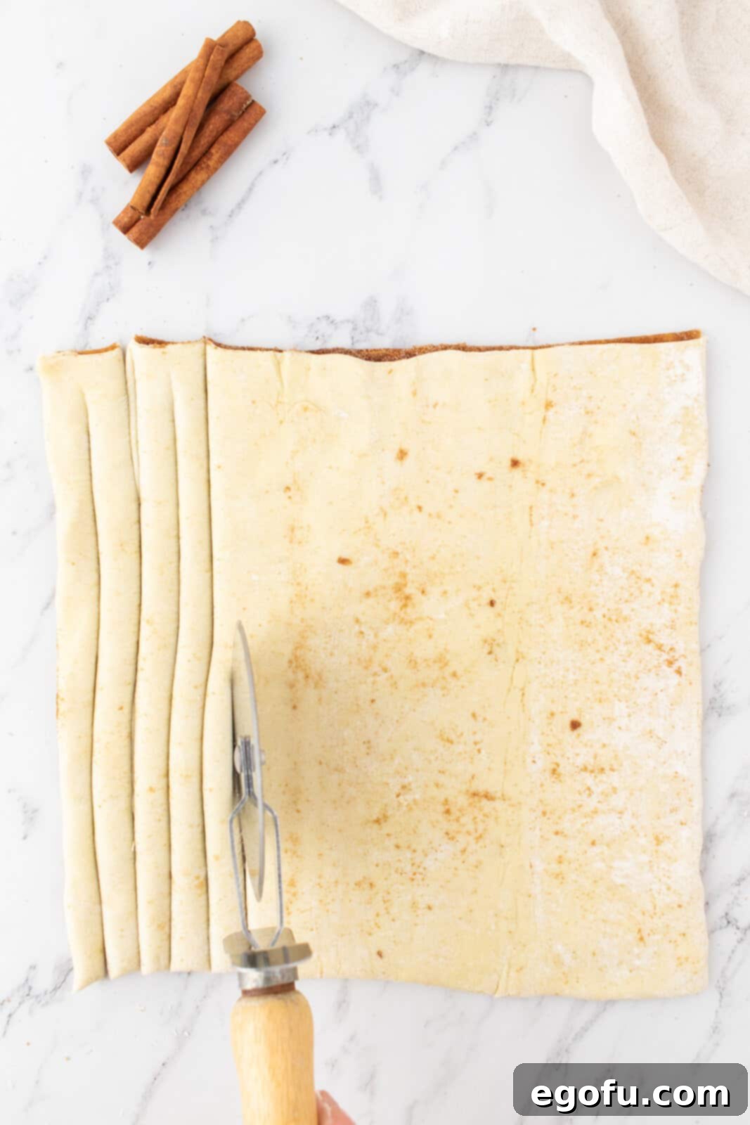 a pizza cutter cutting strips into puff pastry dough.