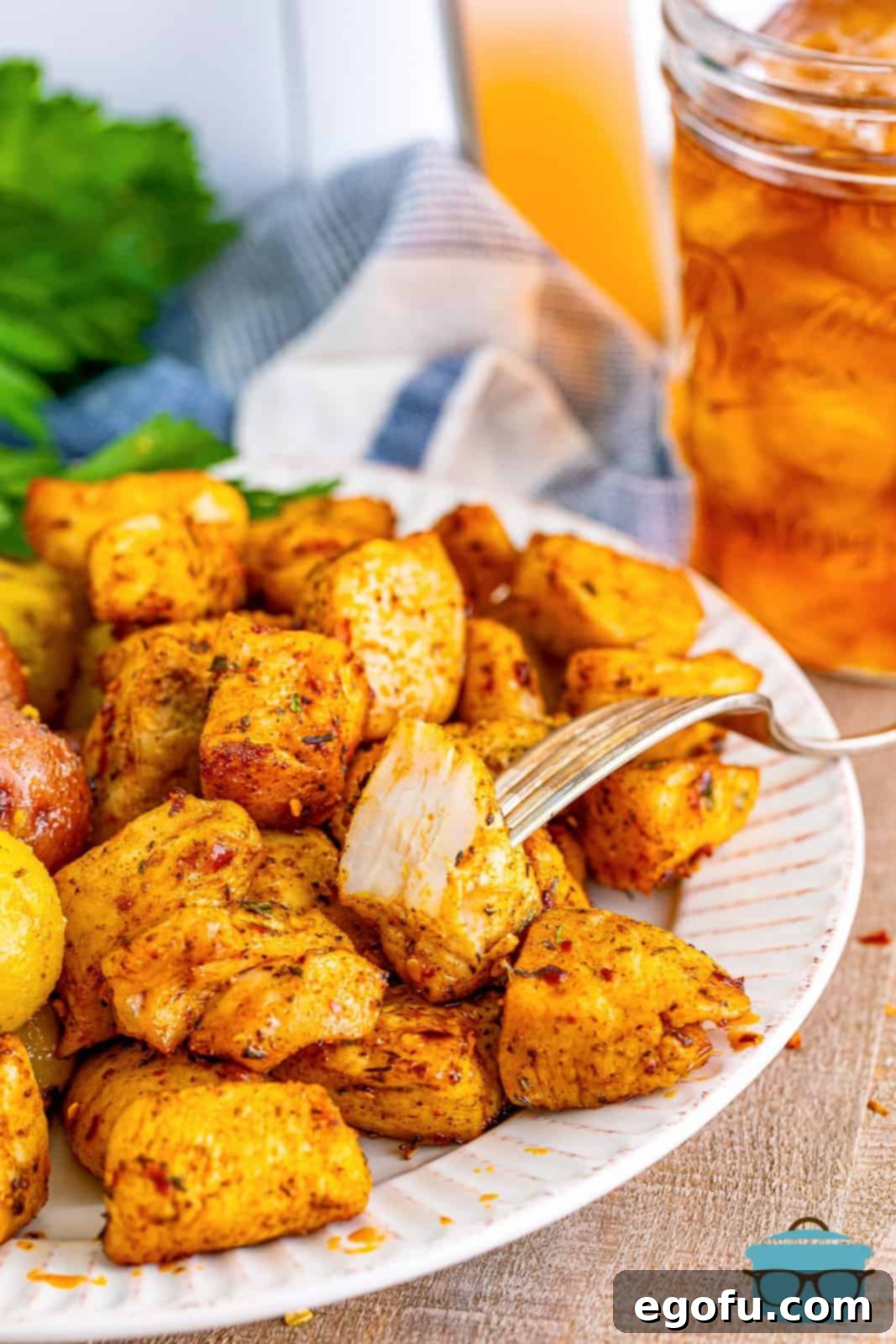 Cooked chicken breast chunks displayed artfully on a white plate, with a refreshing mason jar of iced tea visible in the soft background. The focus is on the golden-brown chicken, glistening with seasoning, inviting viewers to savor its delicious appearance.