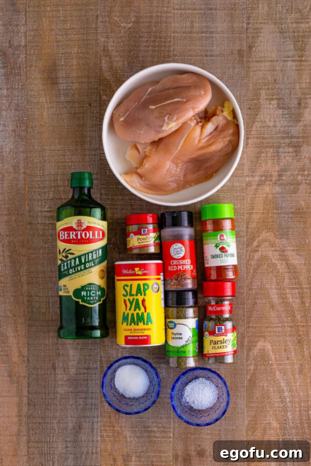 A vibrant flat lay showcasing all the essential ingredients for Air Fryer Chicken Bites: fresh chicken breasts, a bottle of golden olive oil, various seasoning containers including Cajun seasoning, salt, smoked paprika, red pepper flakes, poultry seasoning, and a small pile of dried thyme, all ready for preparation.