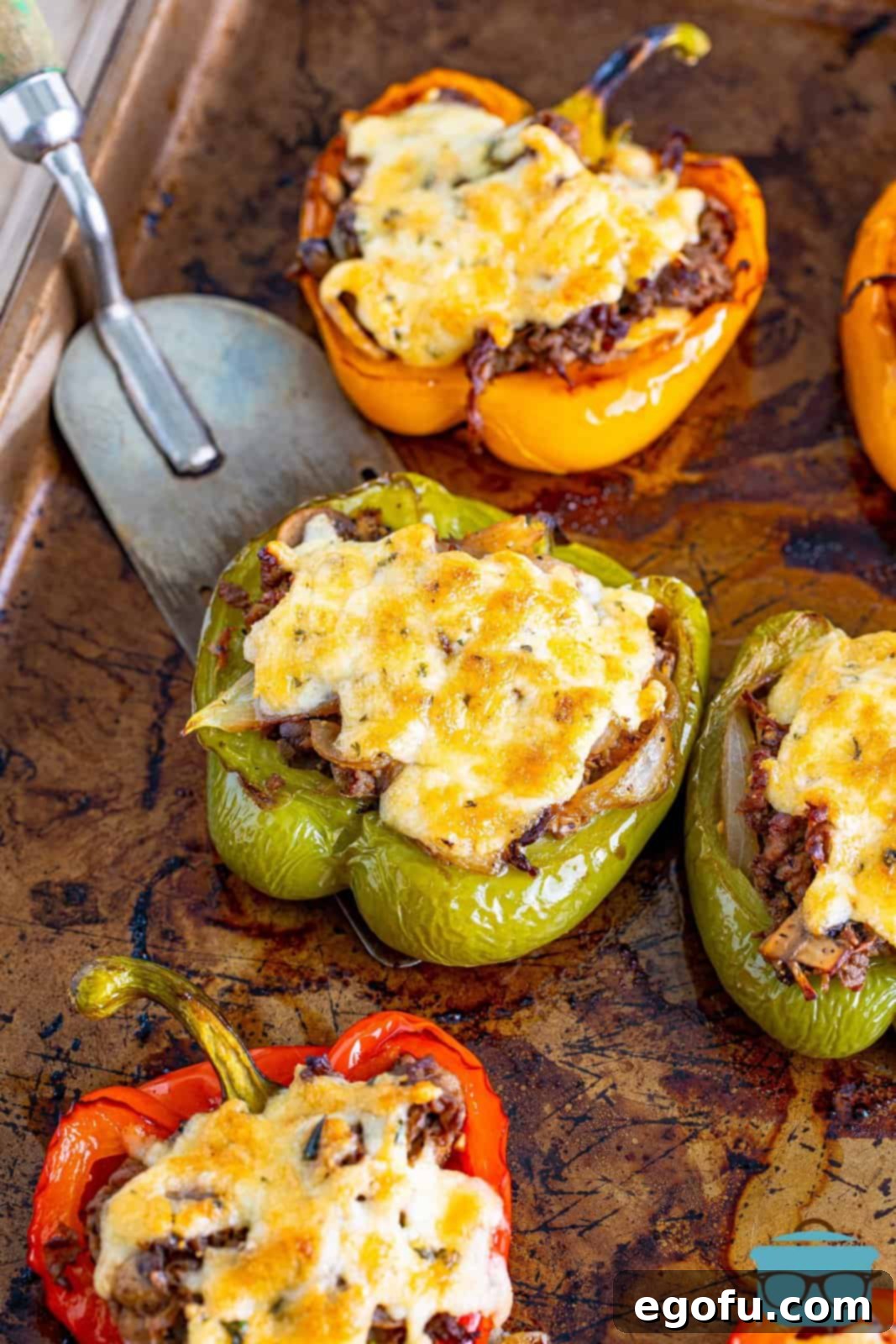 Philly Cheesesteak Pepper Boats 15 fully baked cheesesteak stuffed peppers on a baking sheet with a spatula scooping out one of the green peppers on the tray.