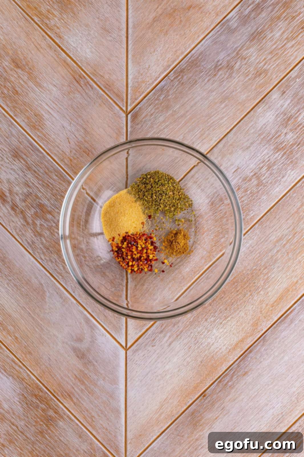 Dried spices are carefully added to a clear glass bowl, ready for mixing.