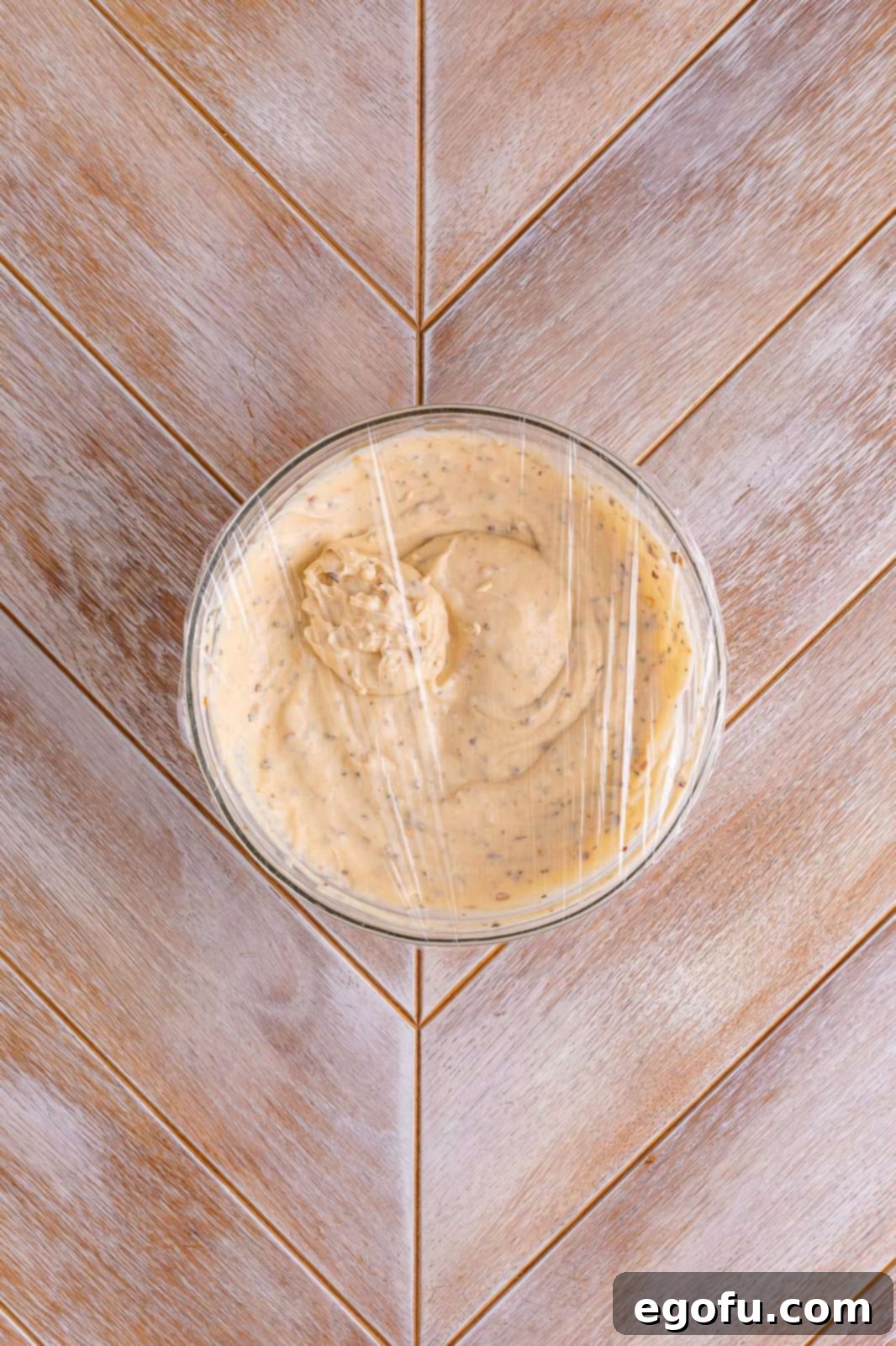 A bowl of freshly mixed white salsa is covered with plastic wrap, ready to be refrigerated for chilling.