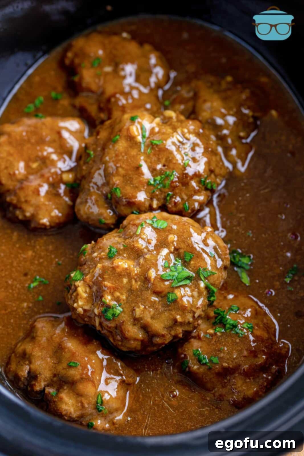 fully cooked patties with thickened gravy in a slow cooker with freshly topped parsley on top.