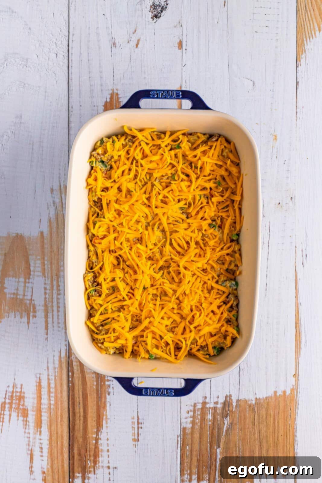 A baking dish with a casserole mixture inside and topped with shredded cheese.