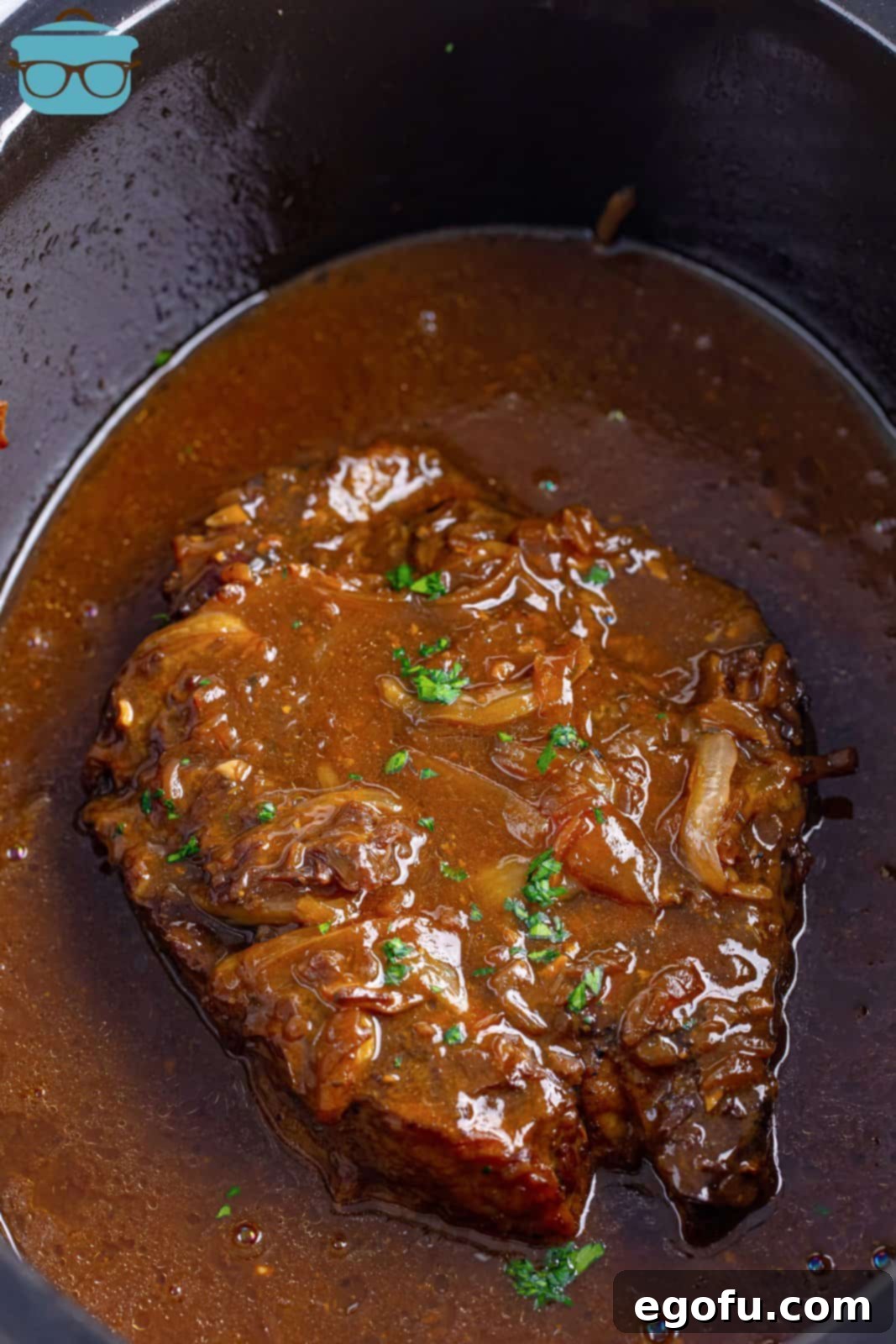 Looking down on a crockpot filled to the brim with ready-to-serve French Onion Pot Roast and its savory gravy.