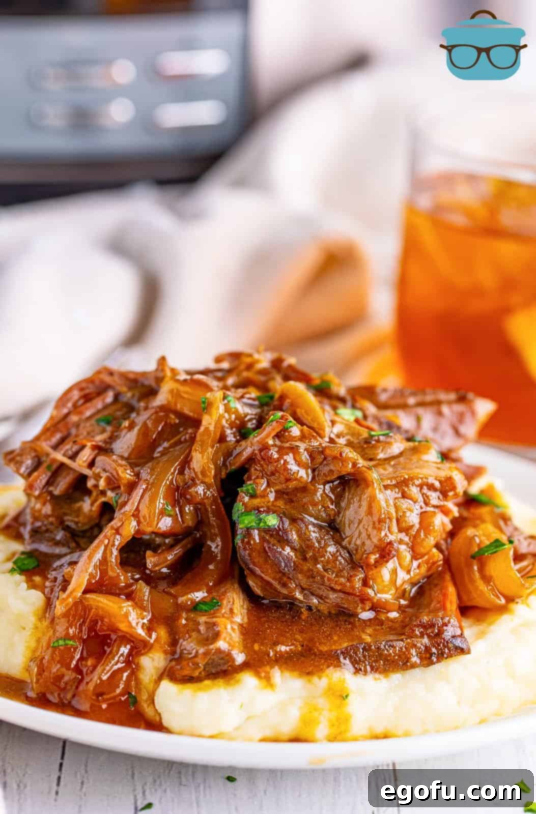 A generous serving of Slow Cooker French Onion Pot Roast, beautifully plated over a bed of mashed potatoes and garnished with fresh parsley.