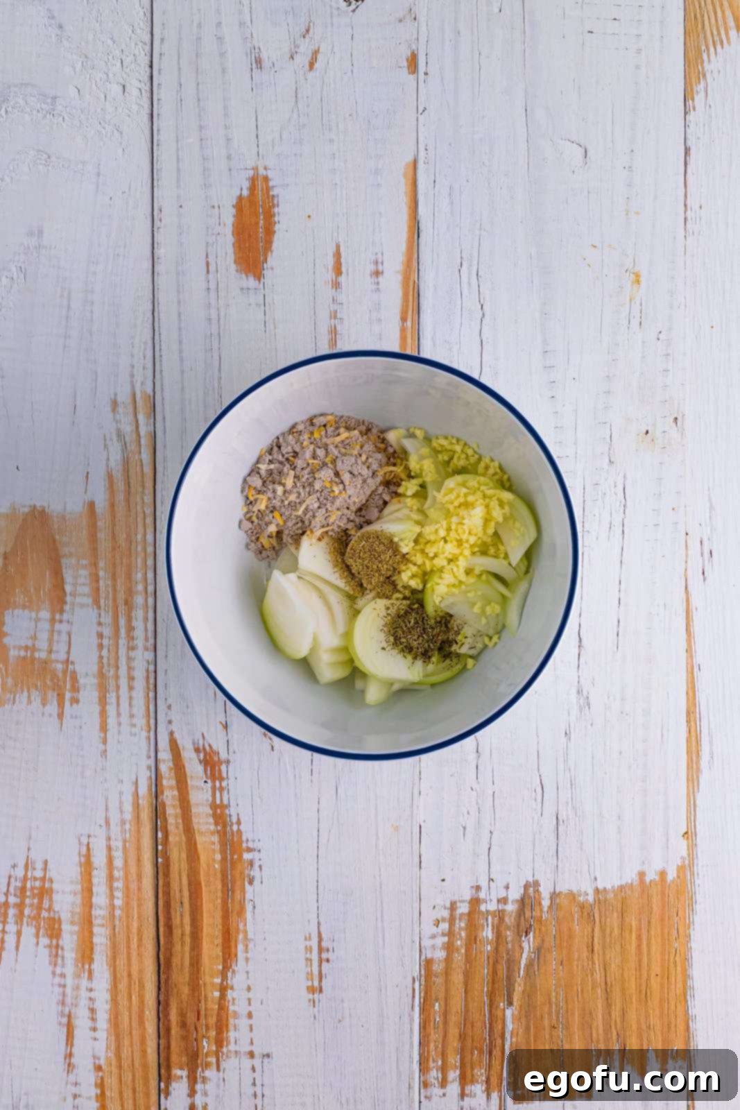 Sliced onions, minced garlic, soup mix, and dried herbs mixed in a bowl, ready for the slow cooker.