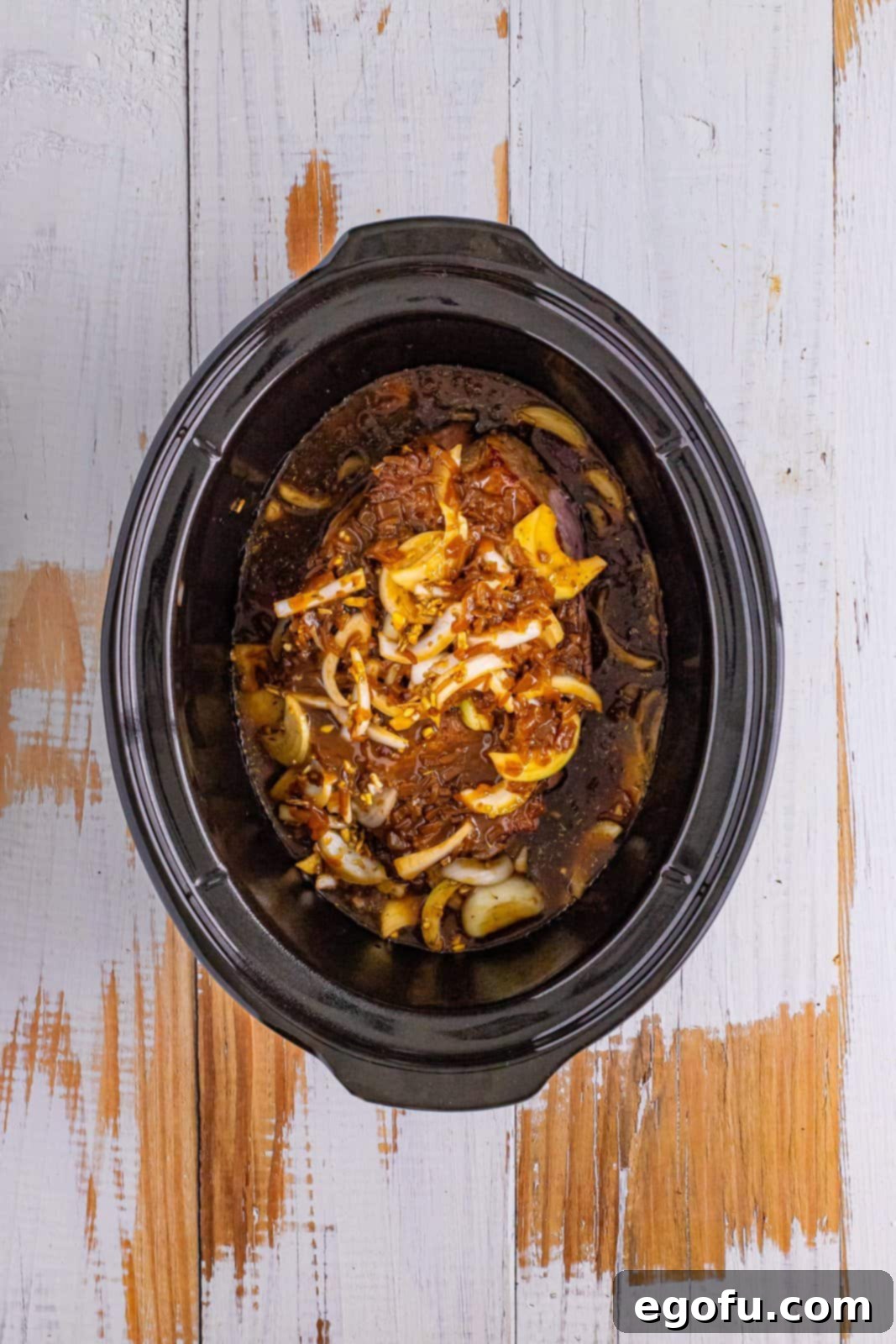 Looking down on a slow cooker with the first layer of onion and herb mixture and one can of condensed French onion soup.