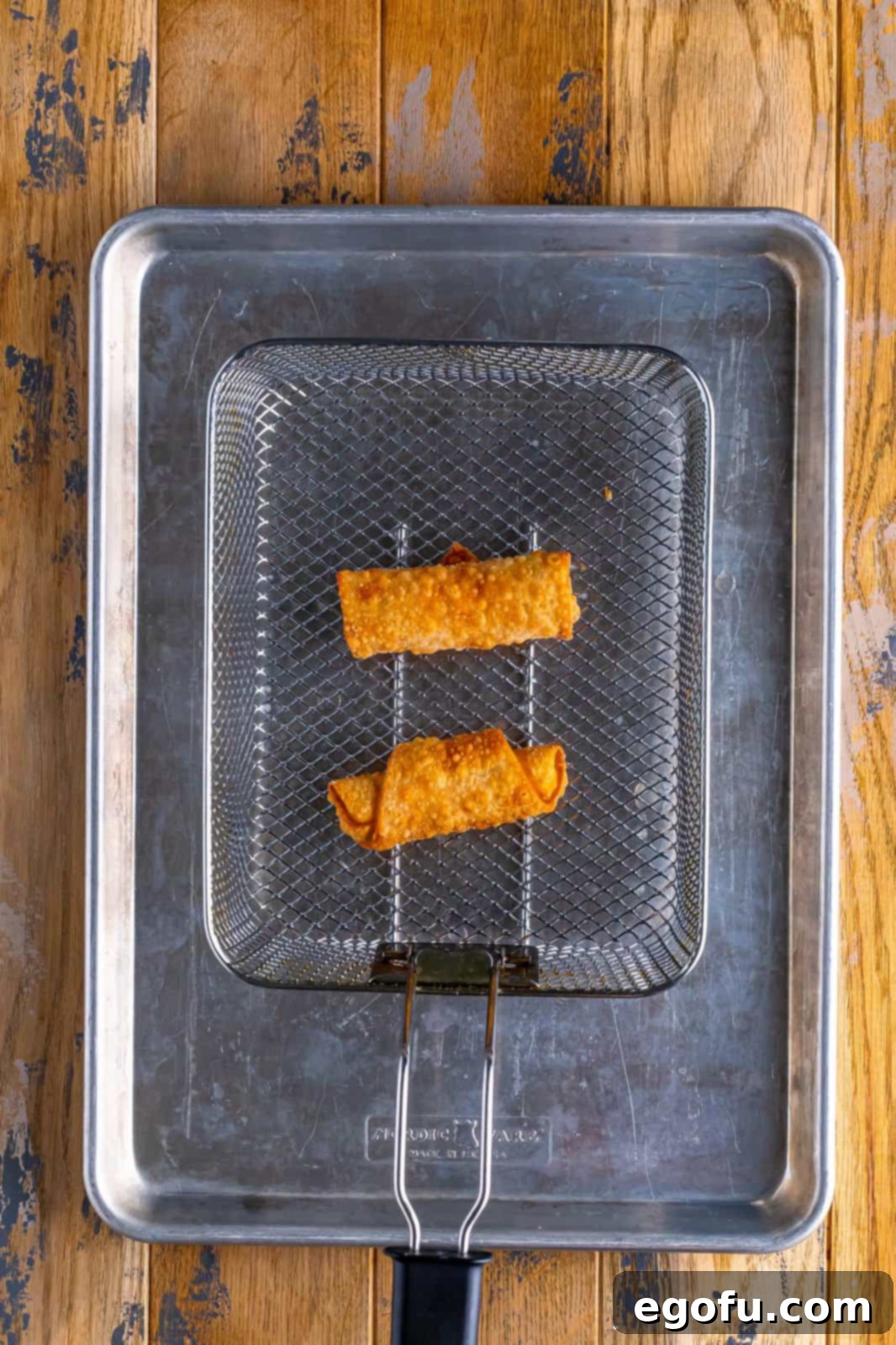 Spicy Creamy Egg Roll Poppers 11 Two Jalapeno Popper Egg Rolls submerged in a frying basket in hot oil.