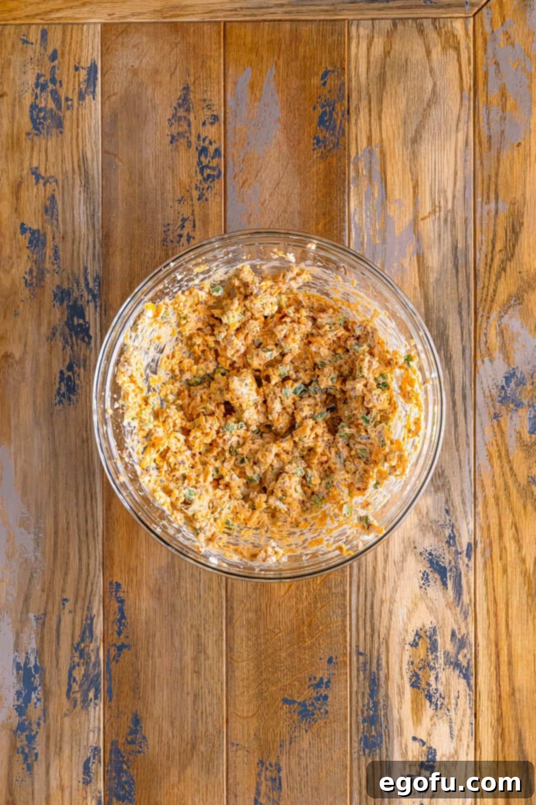 Spicy Creamy Egg Roll Poppers 6 A glass bowl with cream cheese, cheddar, jalapeños, bacon bits, scallion, garlic powder, onion powder, and paprika all mixed together smoothly.