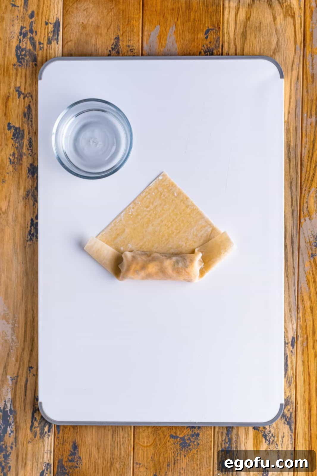 Spicy Creamy Egg Roll Poppers 8 An egg roll wrapper, with filling, starting to be rolled up from the bottom point.