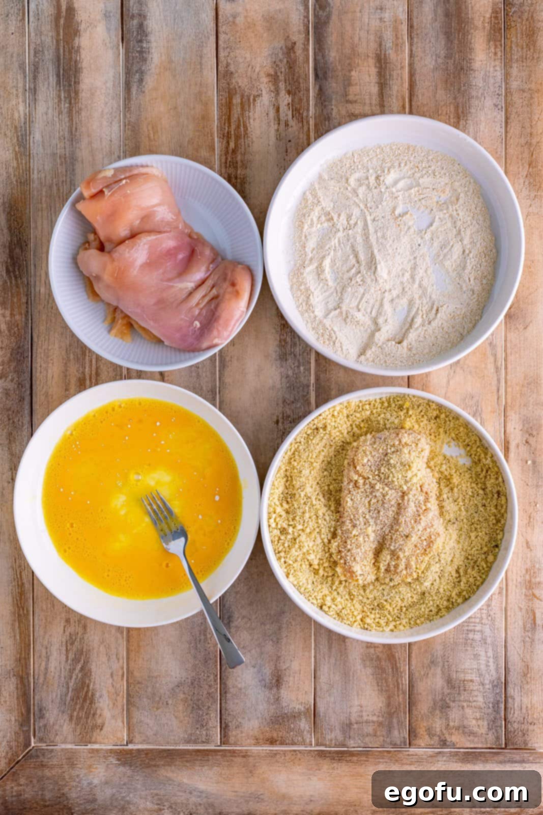 Chicken in a bowl, a bol with egg wash, a bowl with flour mixture, and a final bowl with chicken in the panko breadcrumbs.