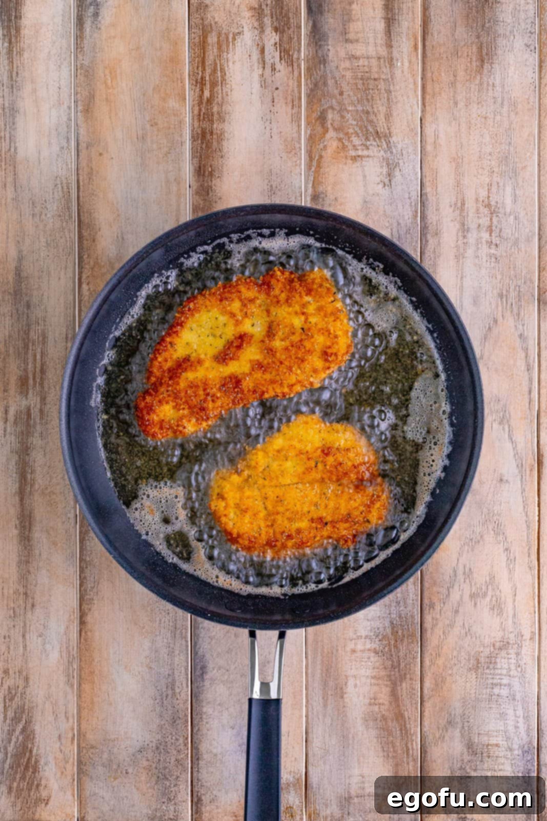 Frying pan with oil and it's frying chicken breasts.