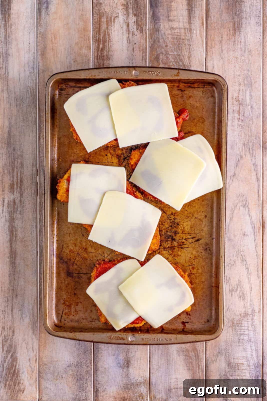 A baking sheet full of breaded fried chicken with tomato sauce and mozzarella cheese slices on top.
