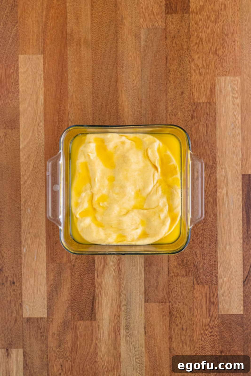 Butter Bathed Cloud Rolls 12 A glass baking dish containing spread-out bread dough with a generous layer of melted butter pooled on top.