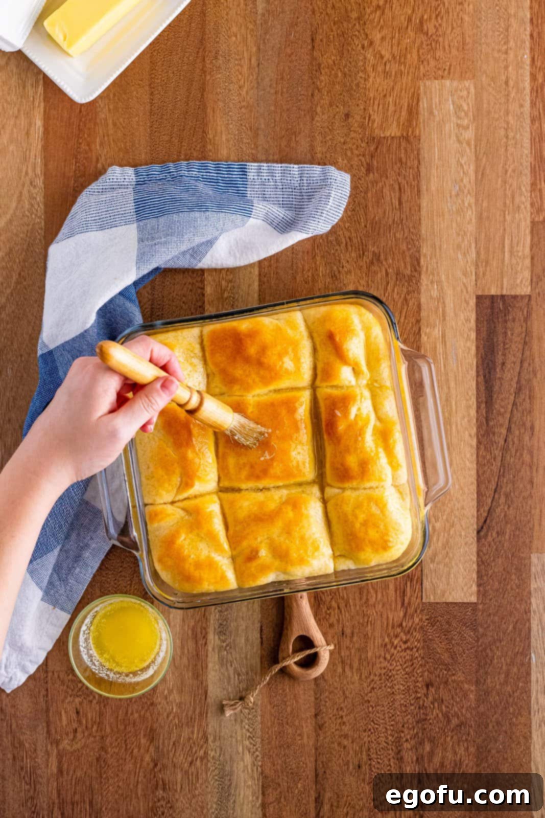 Butter Bathed Cloud Rolls 15 A baking dish showcasing fresh, hot butter dip yeast rolls, with a pastry brush gently applying additional melted butter to their golden tops.