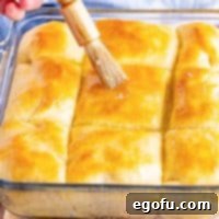 Butter Bathed Cloud Rolls 18 A glass pan of yeast rolls and a pastry brush brushing butter on top.